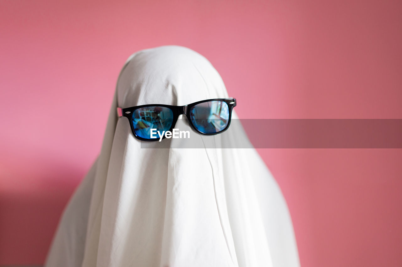 Cute sheet ghost costume with sunglasses on a pink background. halloween party carnival concept.