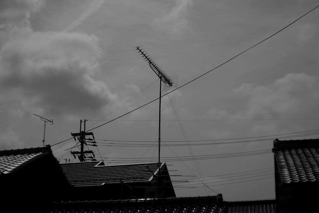 Low angle view of antenna on house roof against cloudy sky