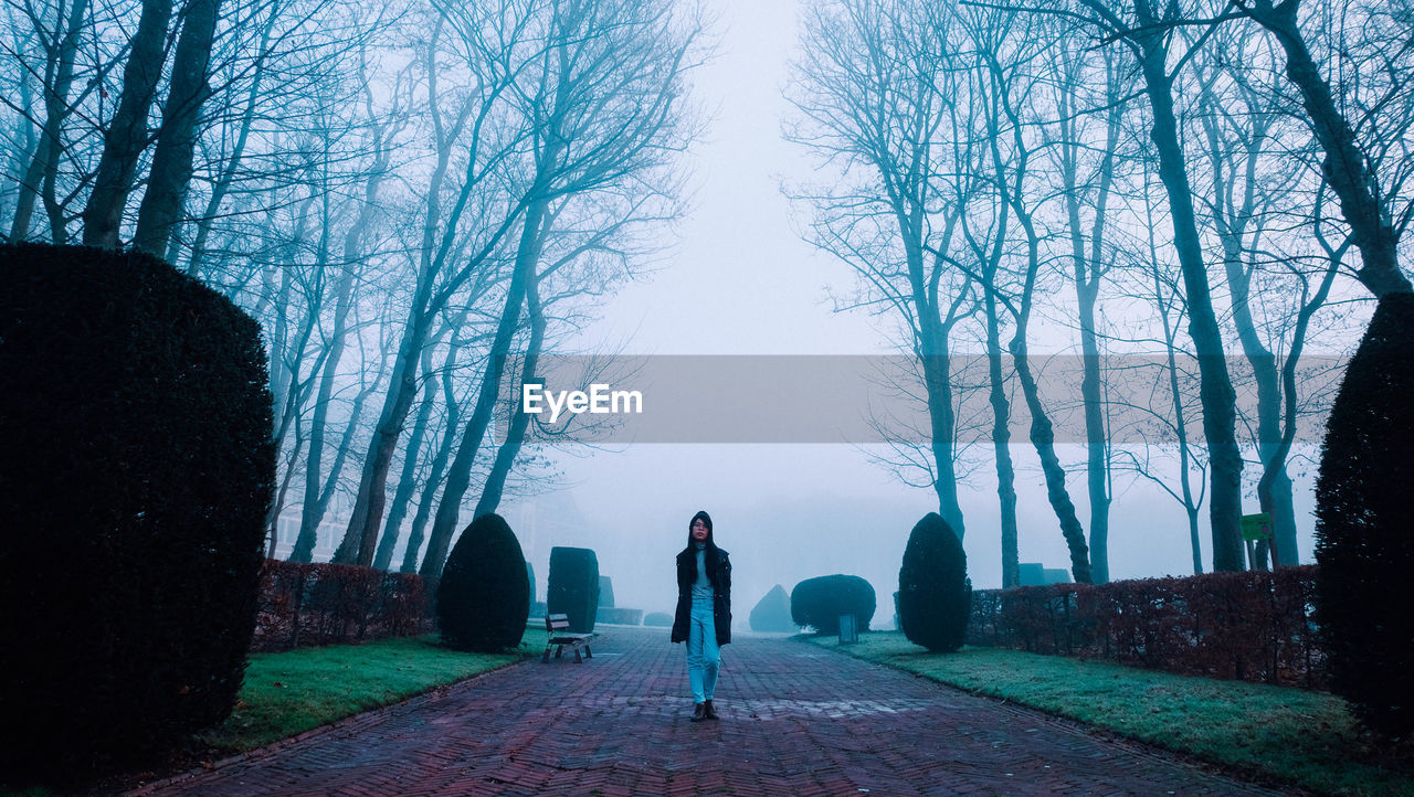 Woman standing on road amidst trees against sky