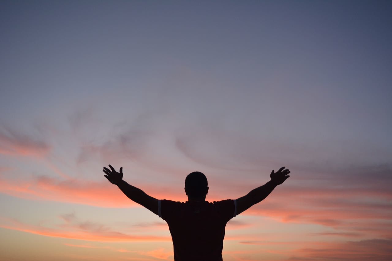 Rear view of man with arms outstretched against sky during sunset