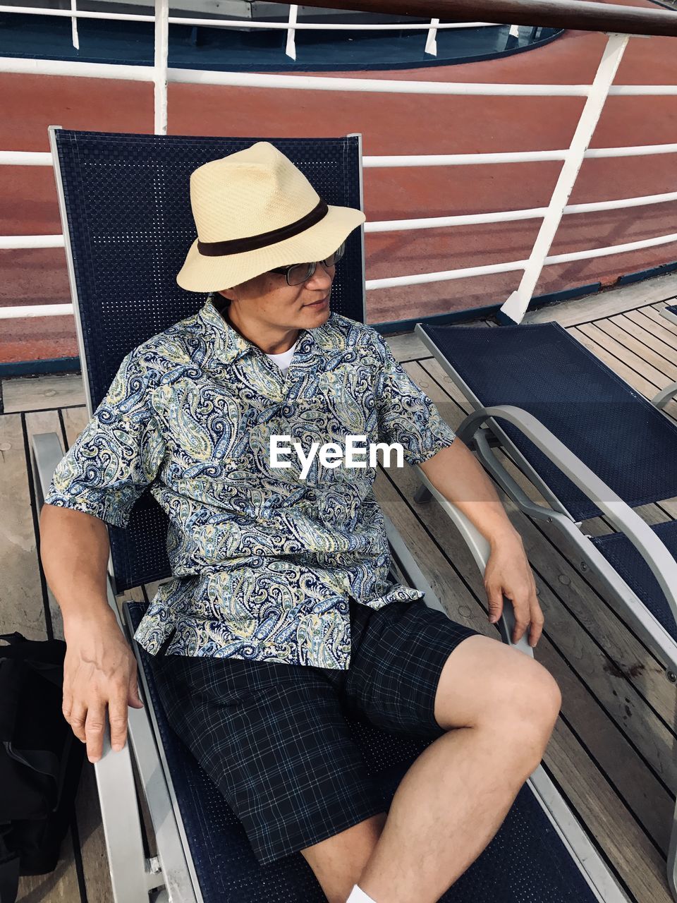 High angle view of man wearing hat sitting on deck chair