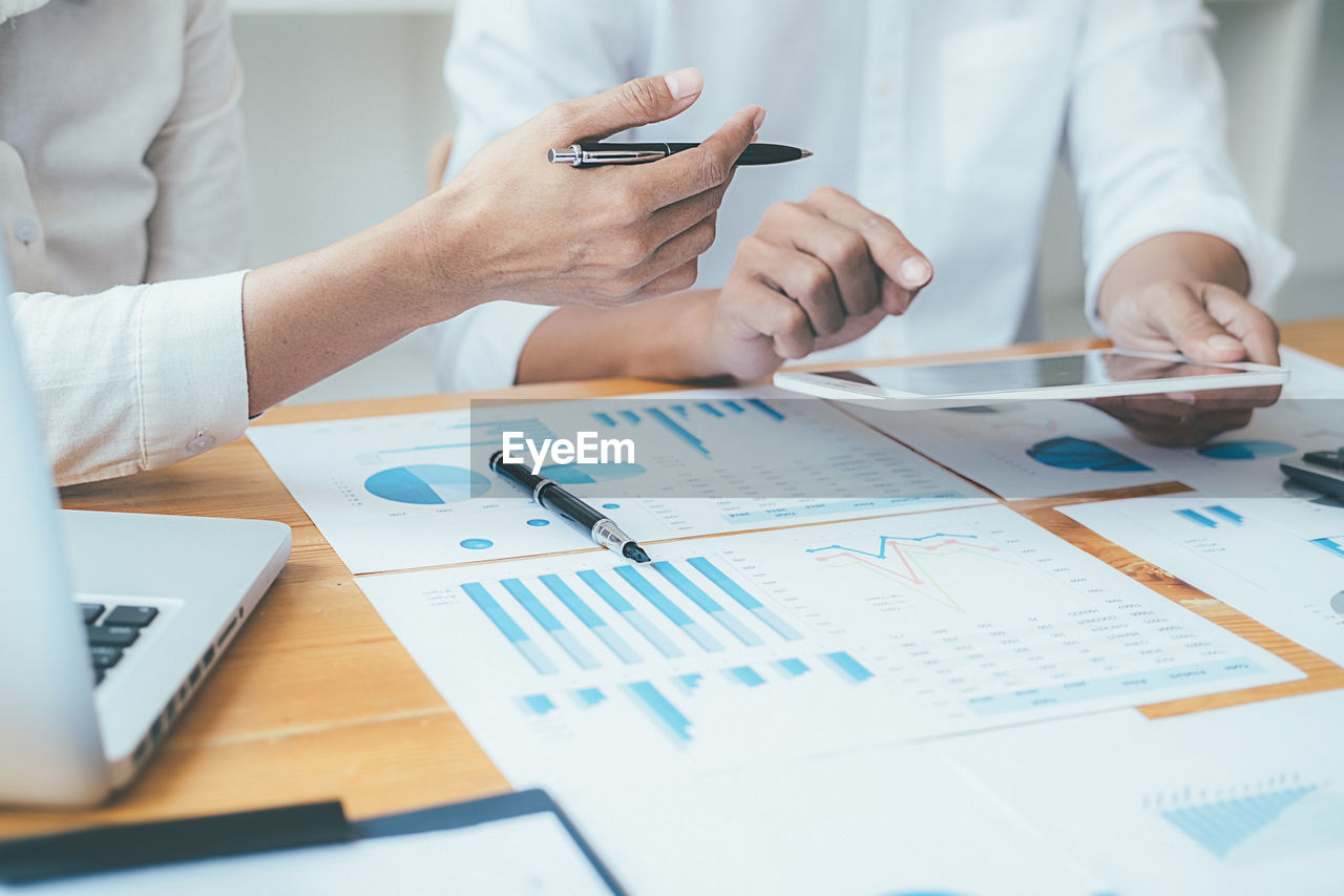 Midsection of businessman and colleague working on table