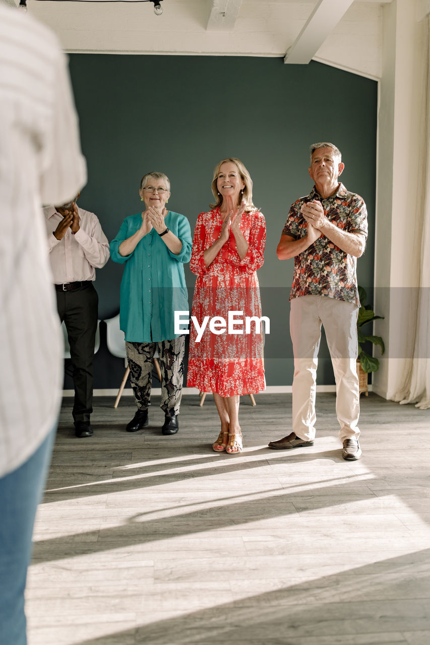 Smiling senior men and women clapping while standing in dance class