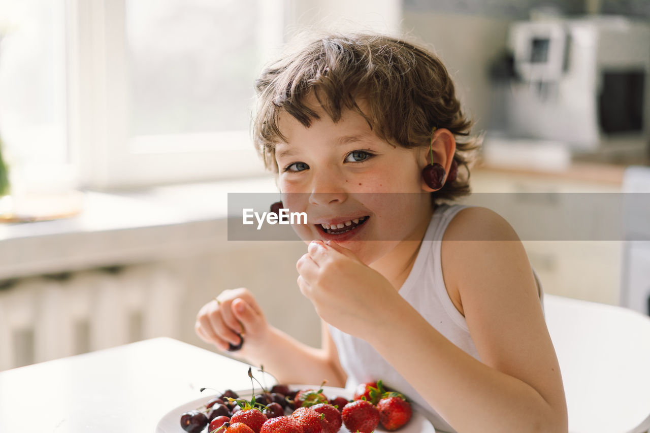 Cute beautiful little boy eating fresh cherry and strawberry.