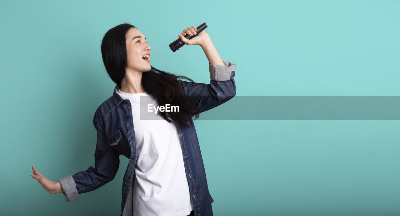 one person, studio shot, adult, colored background, young adult, women, indoors, formal wear, clothing, photo shoot, waist up, person, holding, standing, copy space, long hair, emotion, business, happiness, smiling, outerwear, hairstyle, hand, communication, looking, arm, female, portrait, music, green background