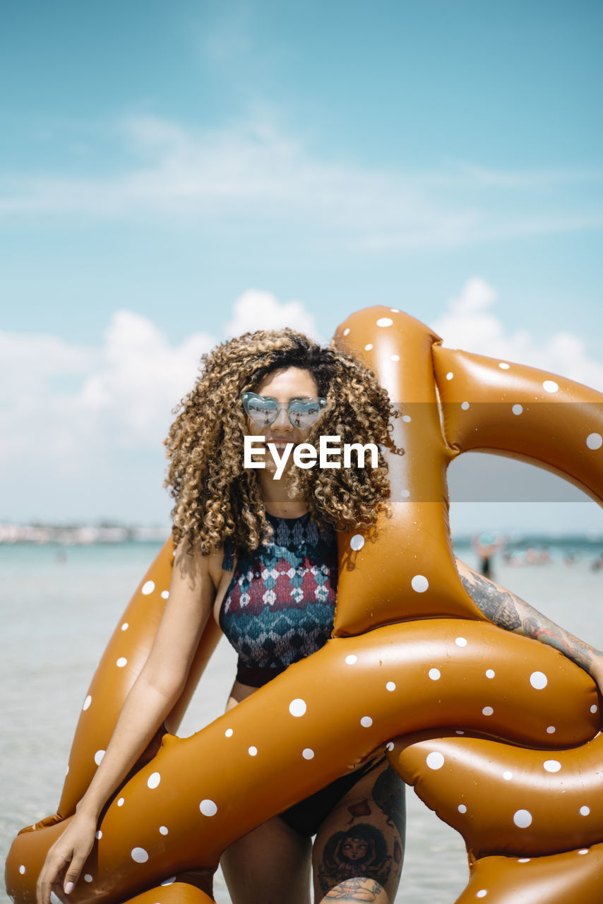 Portrait of smiling woman holding pool raft while standing at beach