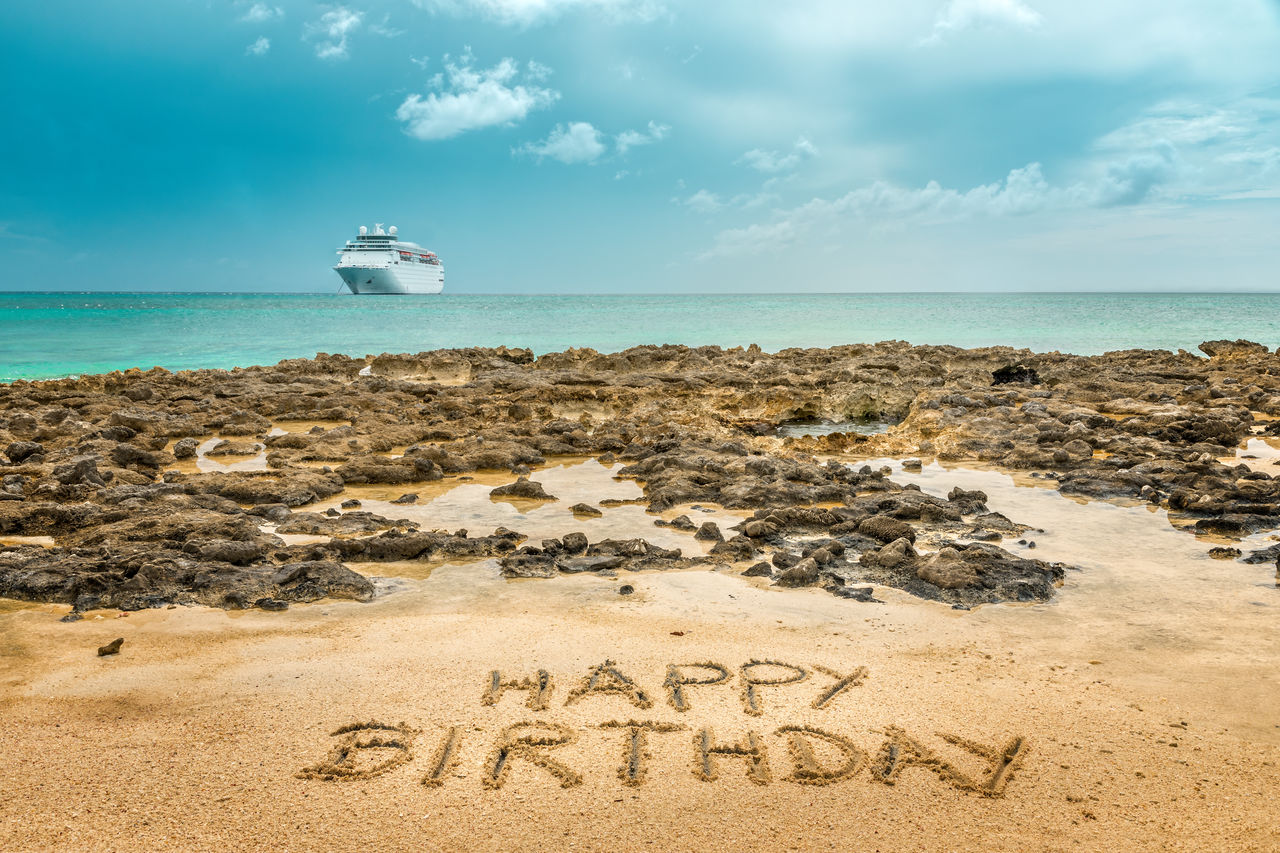 Hand written happy birthday on the sandy beach by the ocean with a cruise ship in the background