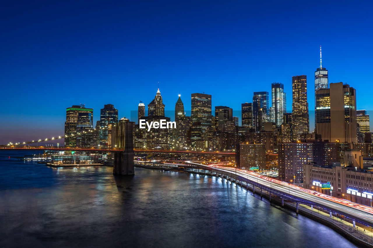 ILLUMINATED BRIDGE OVER RIVER AGAINST BUILDINGS