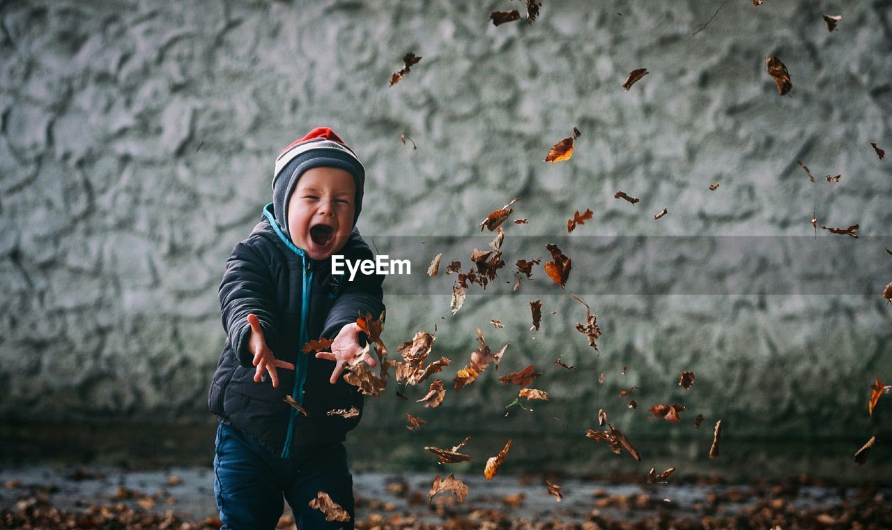 Preschool boy in warm clothing throwing autumn leaves in mid-air