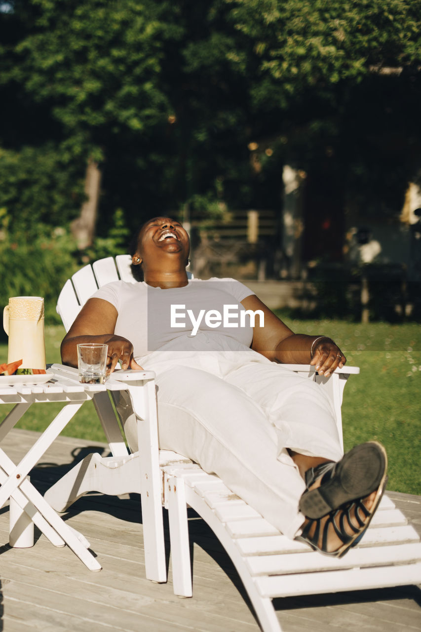 Mid adult woman laughing while sitting on deck chair during garden party