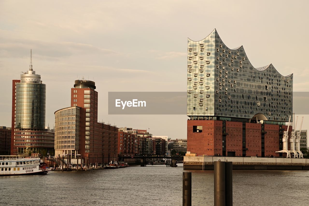 View of buildings by river against sky in city