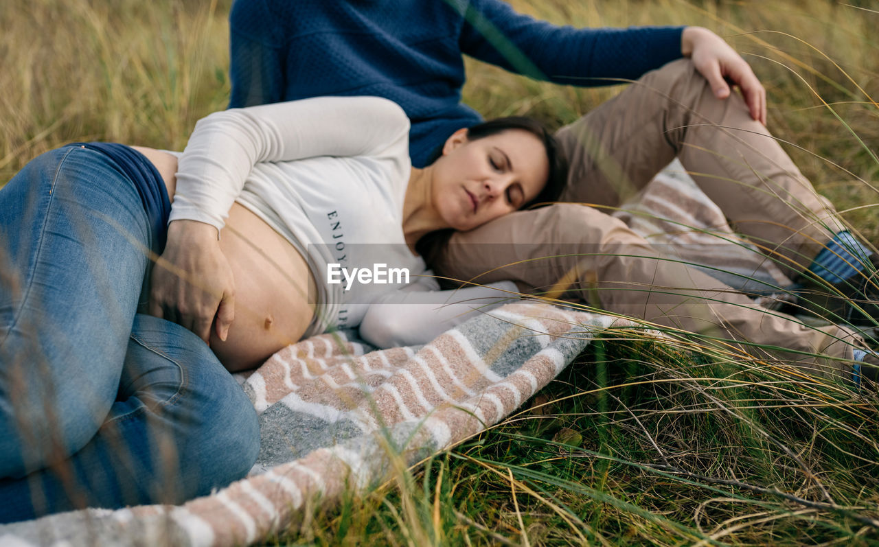 Pregnant woman relaxing with man on field