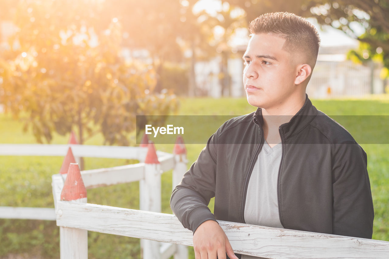 Young male student by the wooden fence thinking about his future and thinking about his business