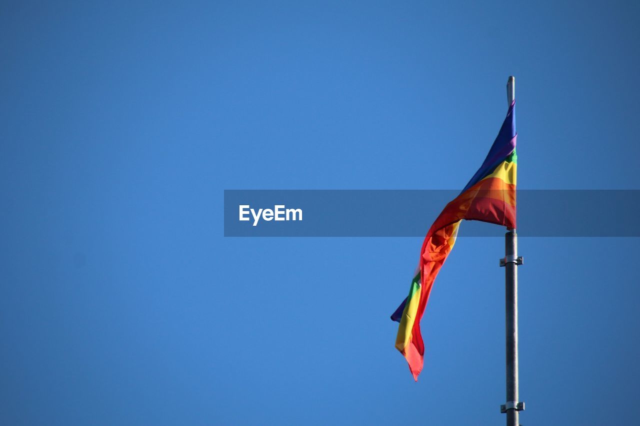 Rainbow flag waving against clear blue sky