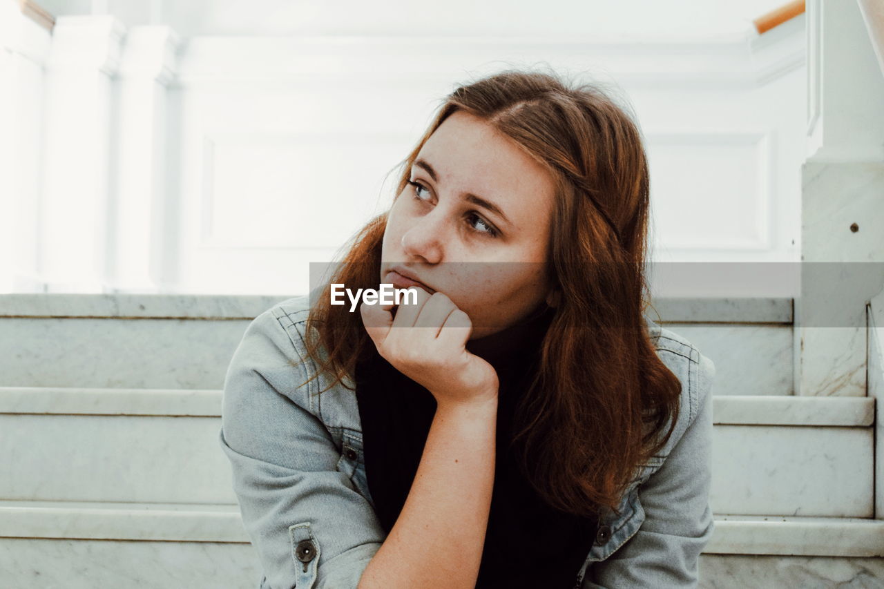 Thoughtful woman with hand on chin sitting on steps