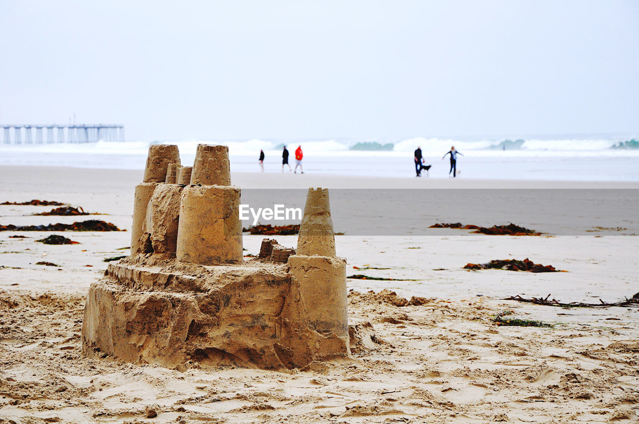 Sandcastle and people at beach against clear sky during winter