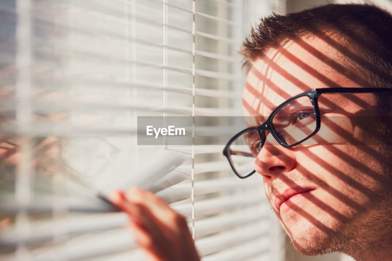 Close-up of young man looking through window at home