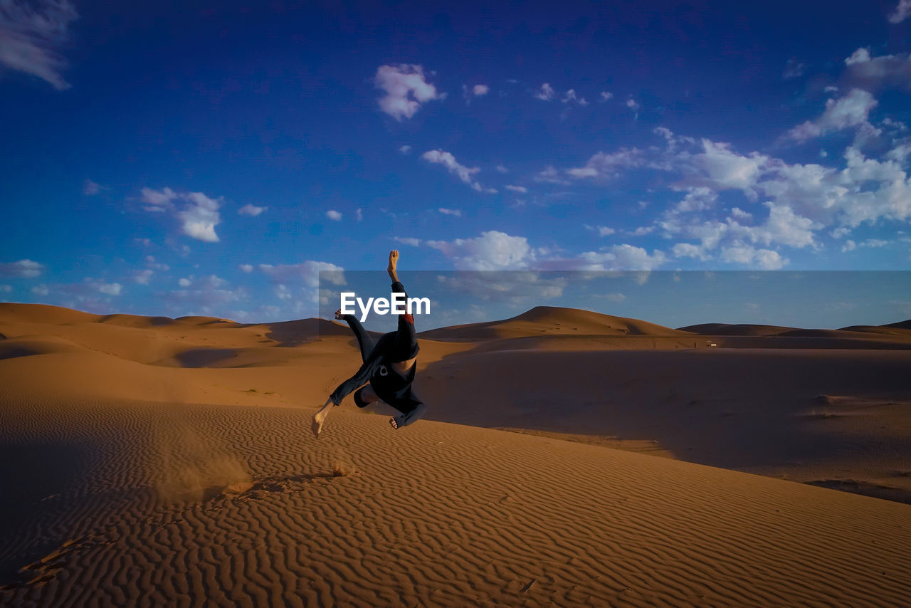 FULL LENGTH OF MAN ON SAND DUNE IN DESERT