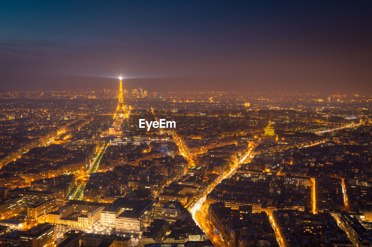 Aerial view of dark night sky above illuminated buildings and roads with high eiffel tower in district of paris