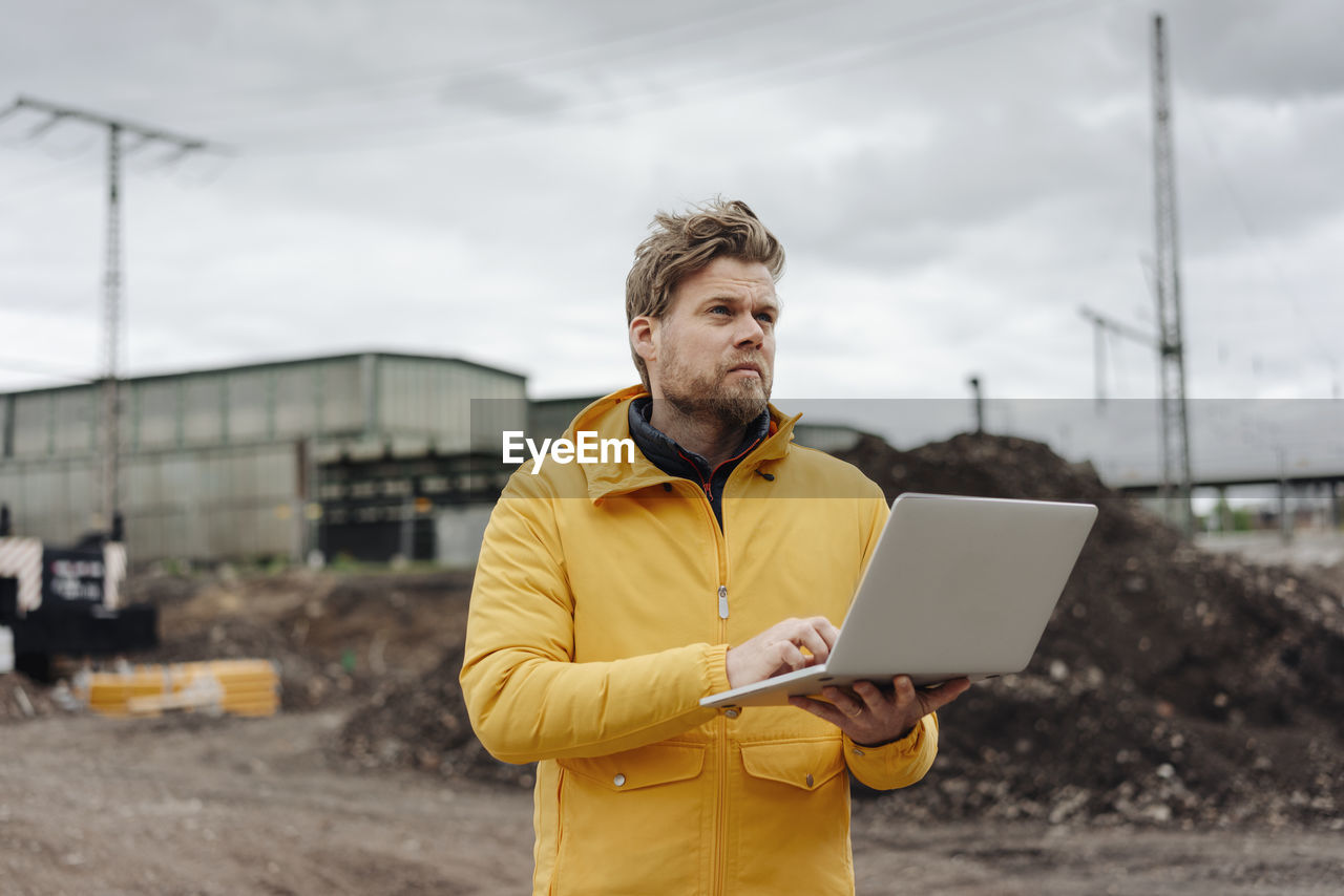 Man holding laptop, construction site in the background