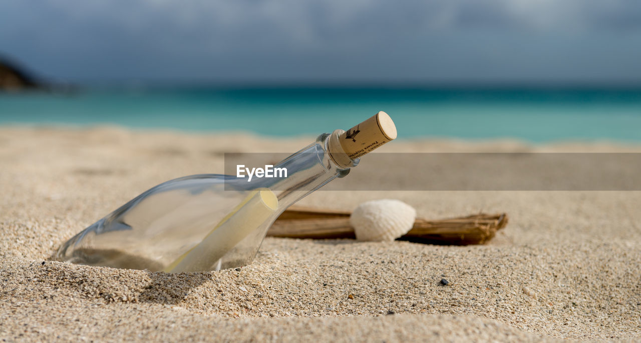 Close-up of message in a bottle on beach against sky