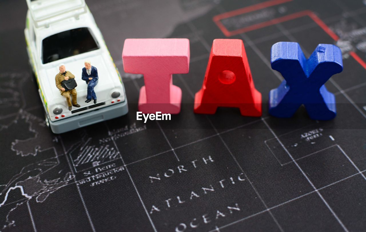 High angle view of tax letter blocks by businessmen toys on map