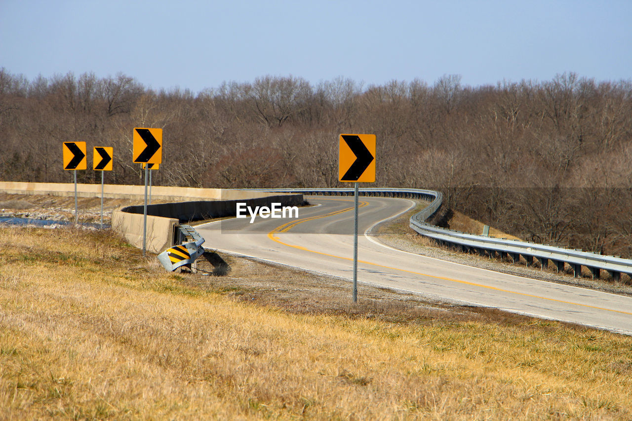 Arrow symbols on empty road against clear sky