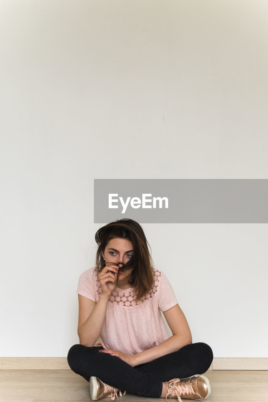 Full length of thoughtful woman sitting on floor against wall at home