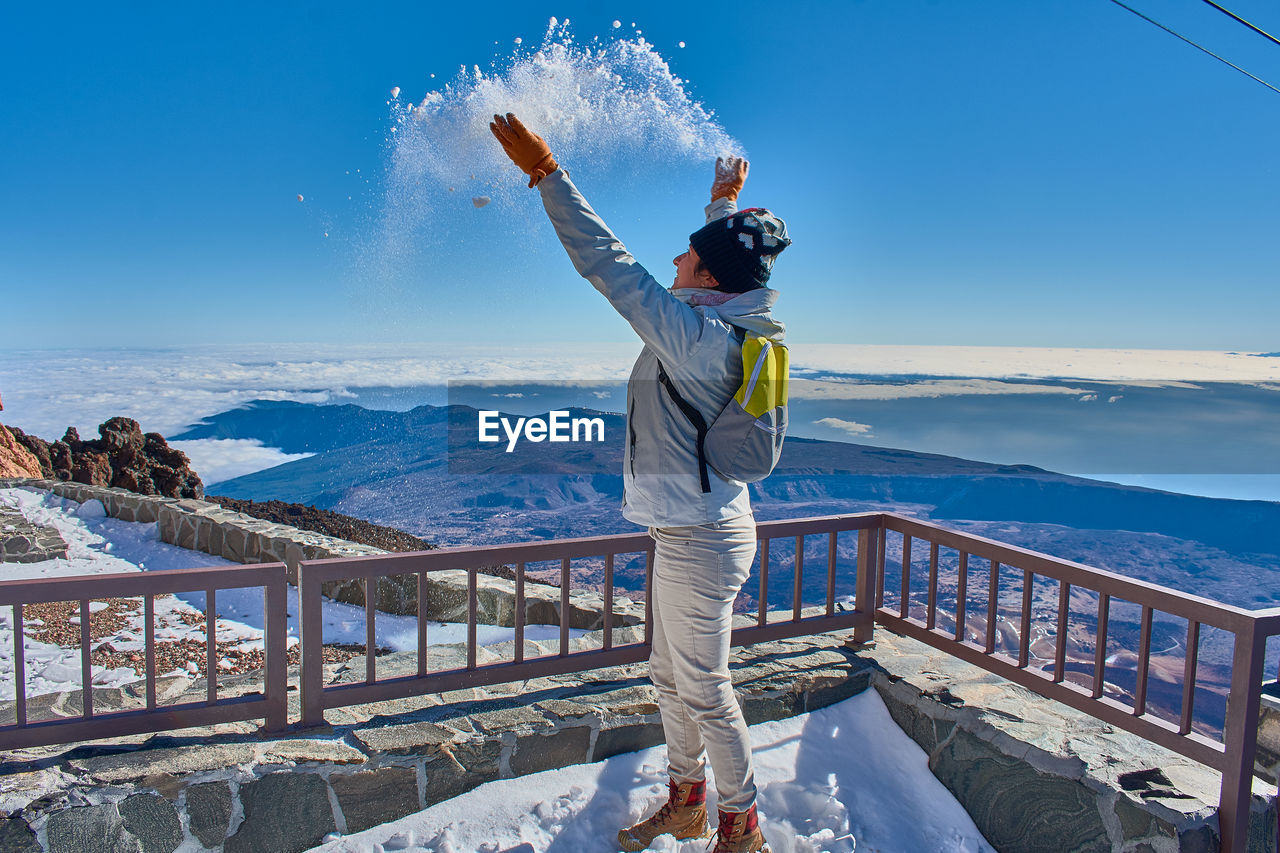 Side view of woman playing with snow on snowcapped mountain