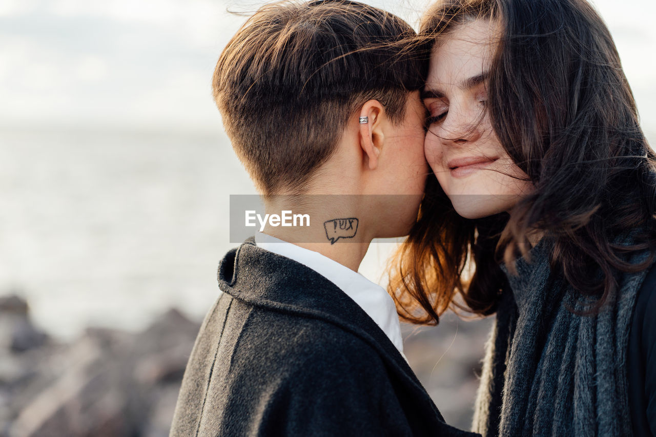 Lesbian women embracing while standing against sea