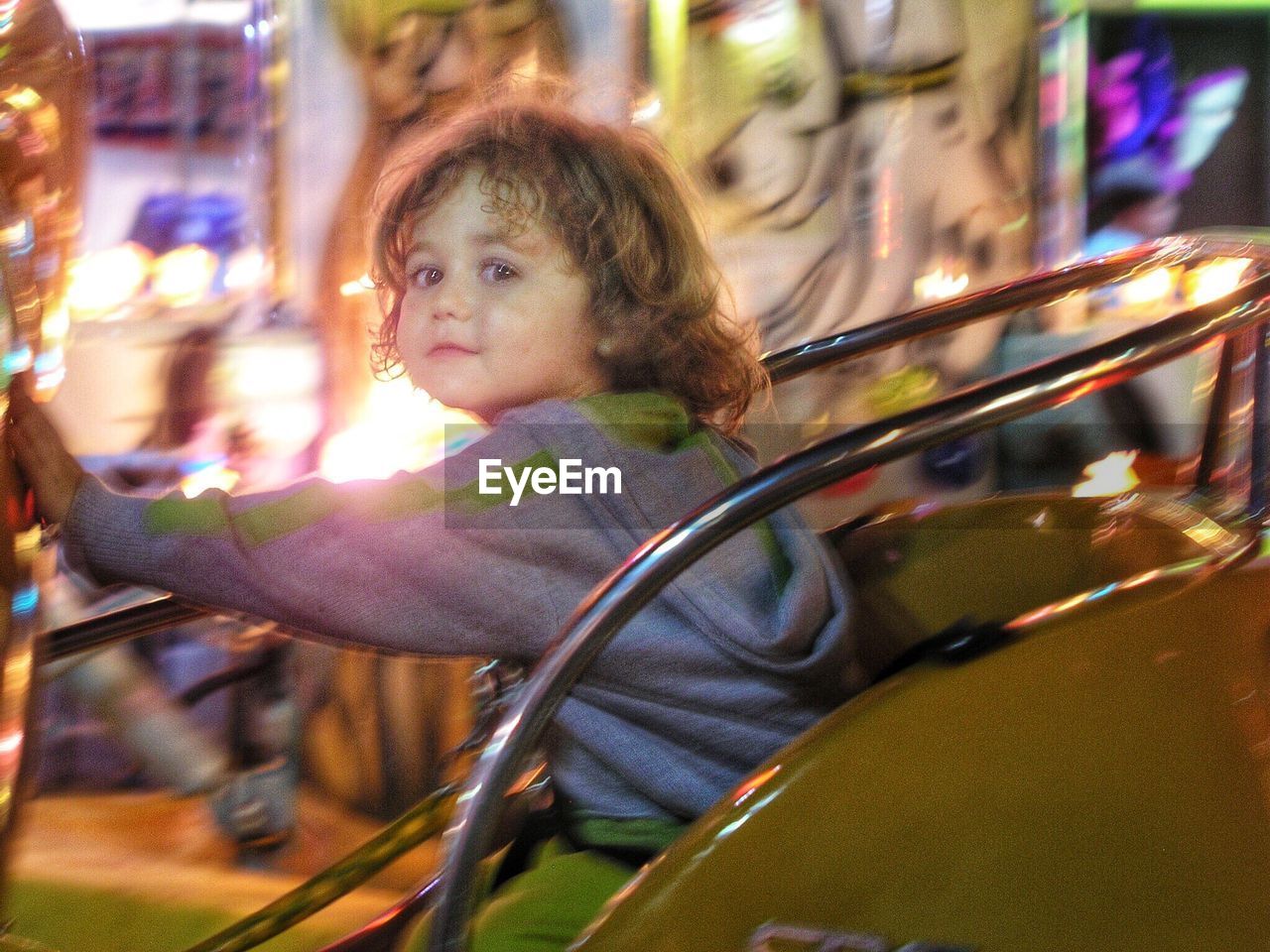 Portrait of cute girl sitting on amusement park ride at night