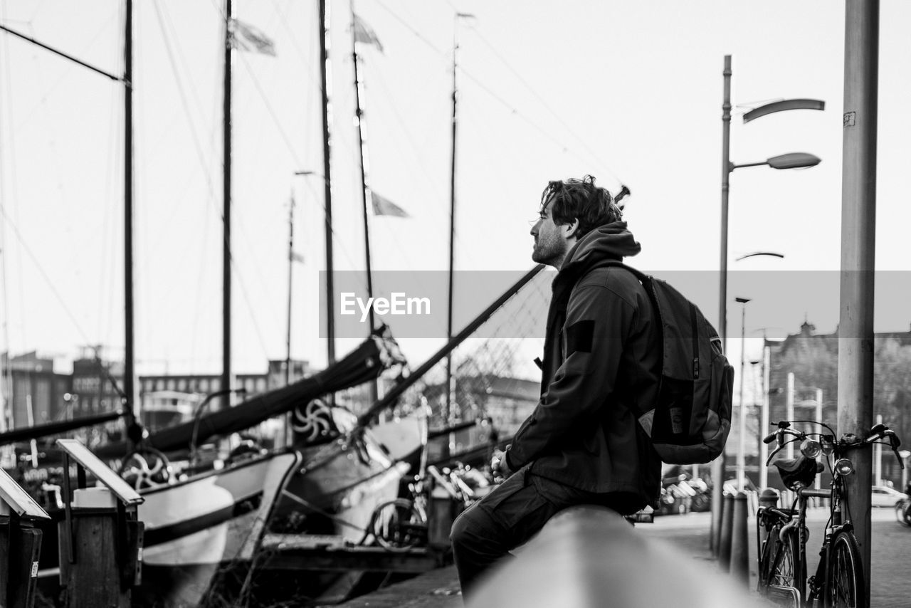 Man sitting on shore against sky in city