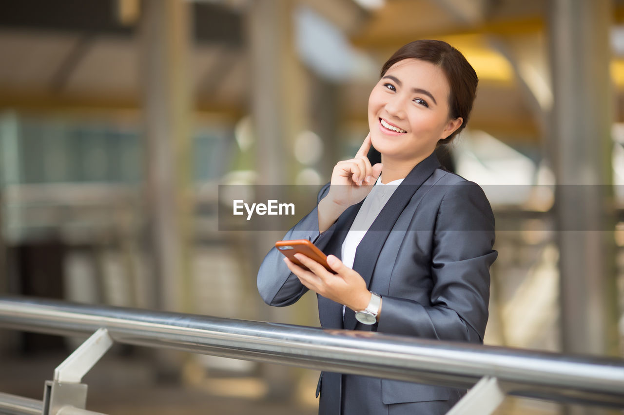 Portrait of smiling businesswoman using mobile phone on bridge in city