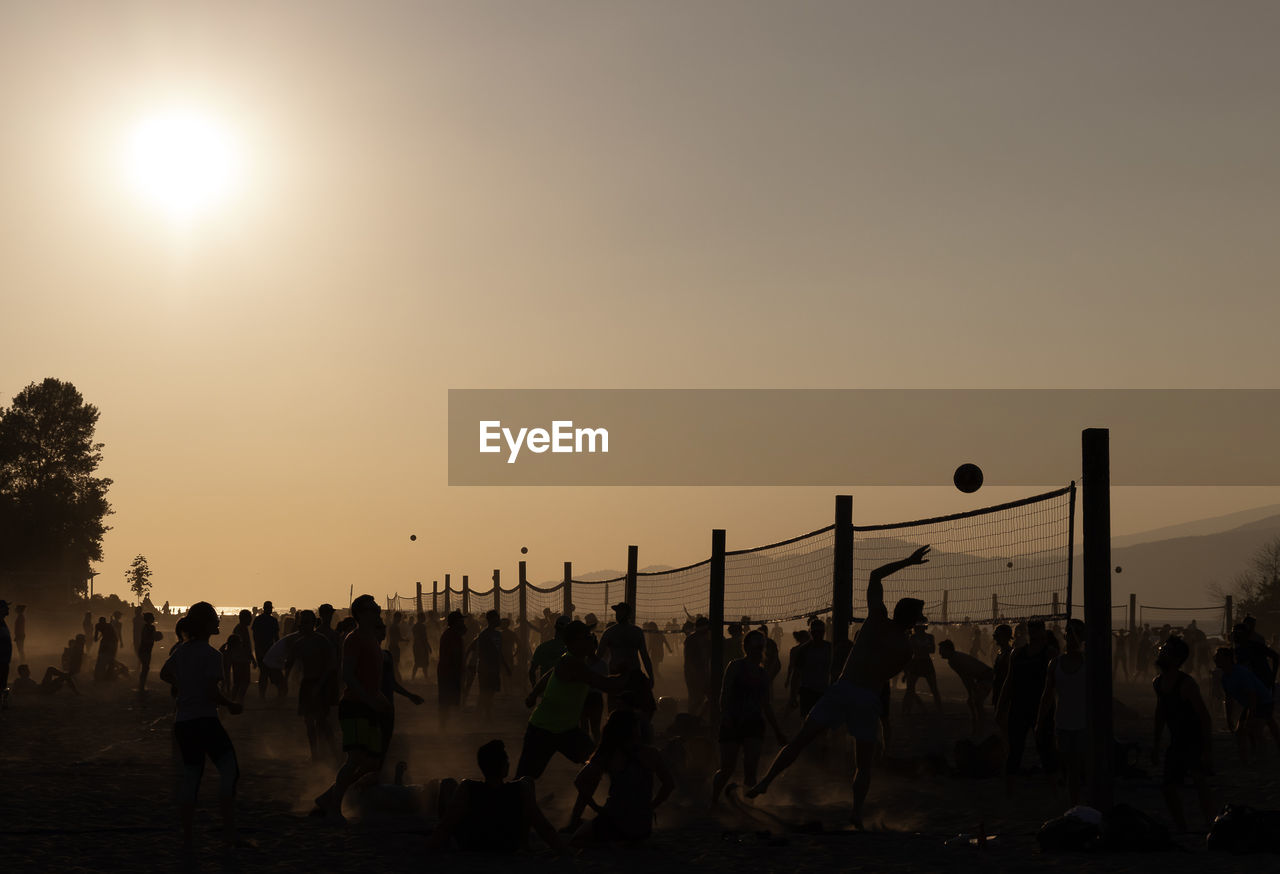 Silhouette people playing volleyball at beach during sunset