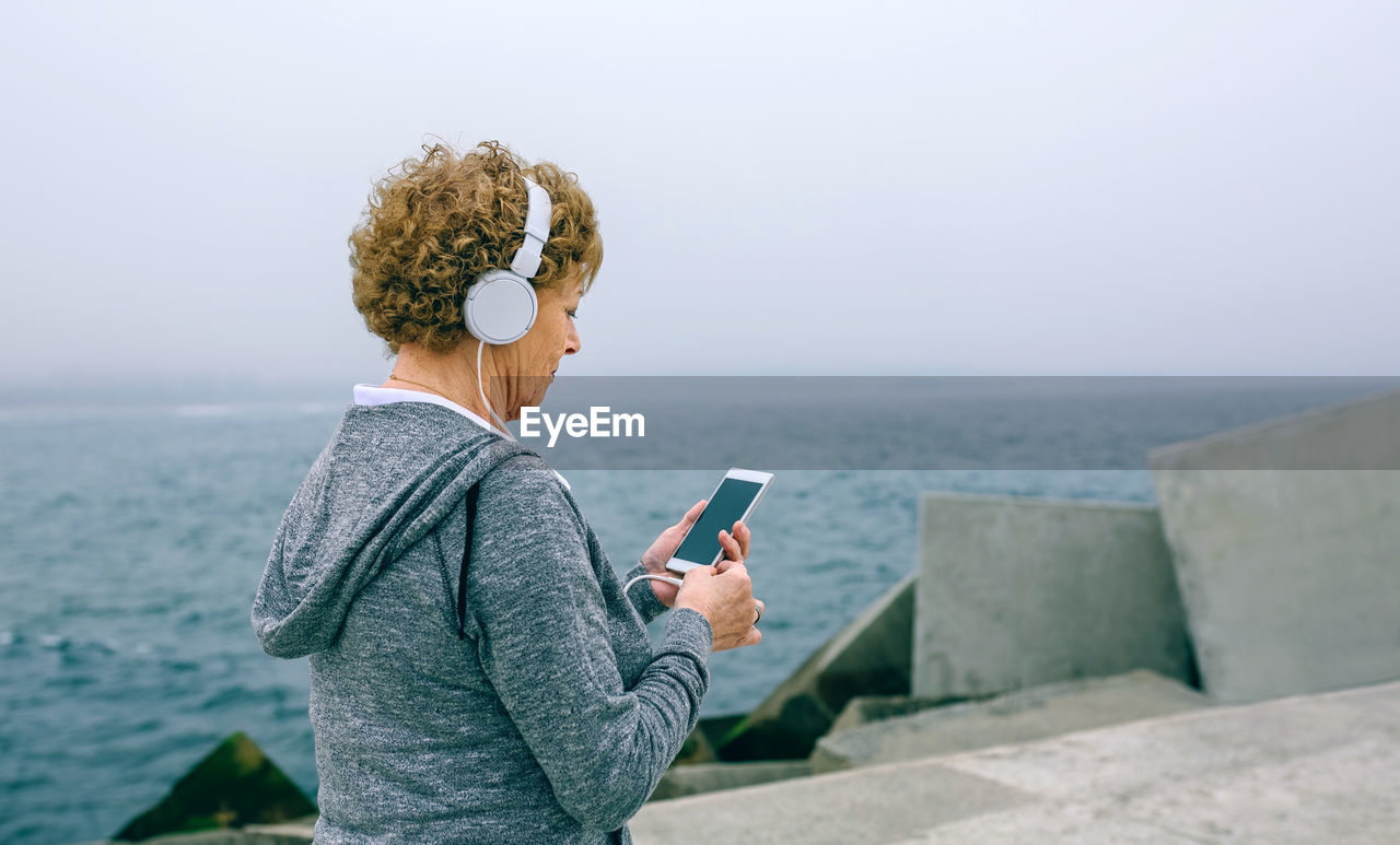 Woman using mobile phone while standing at beach against sky