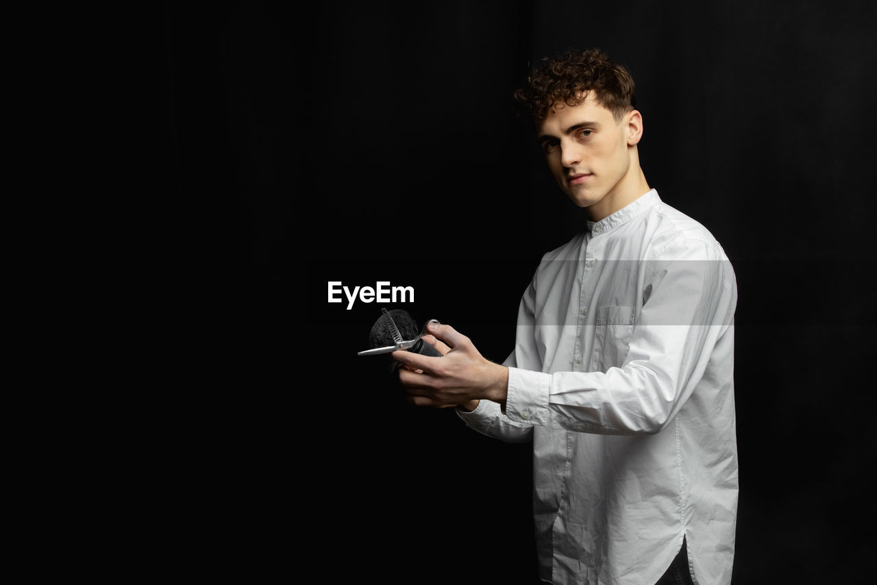 Portrait of male hairdresser with scissor by black background