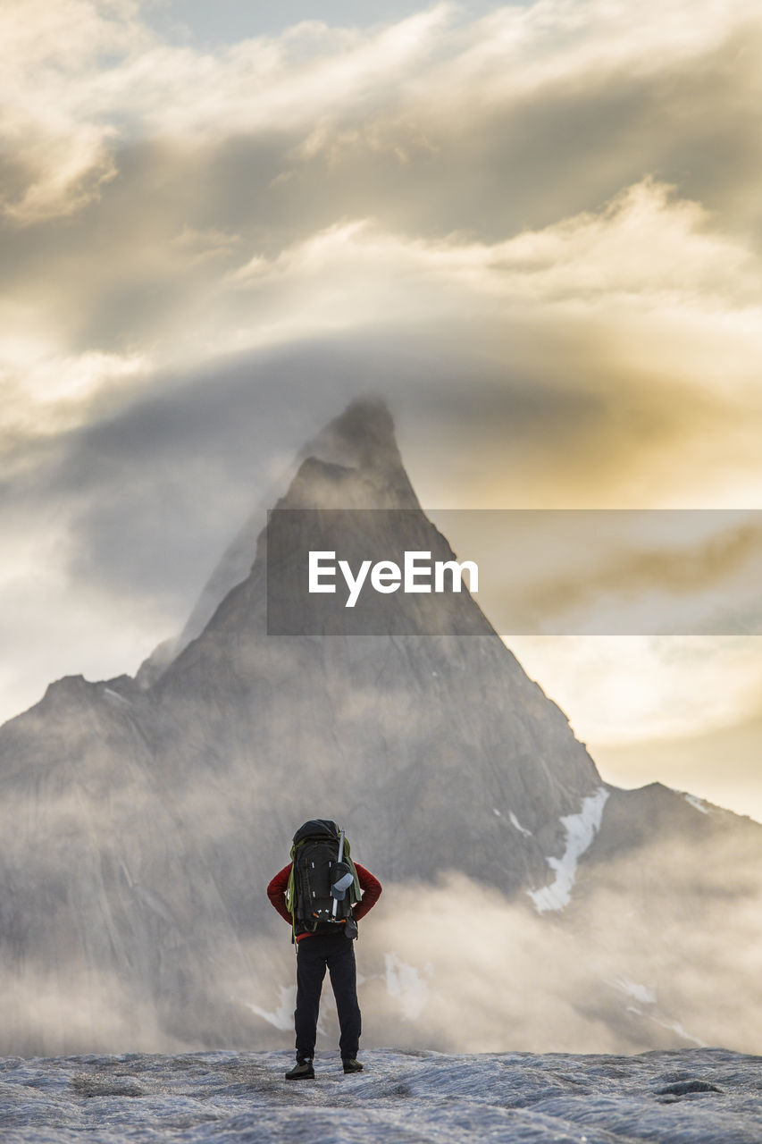 Climber standing in front of mt. loki, baffin island, canada.