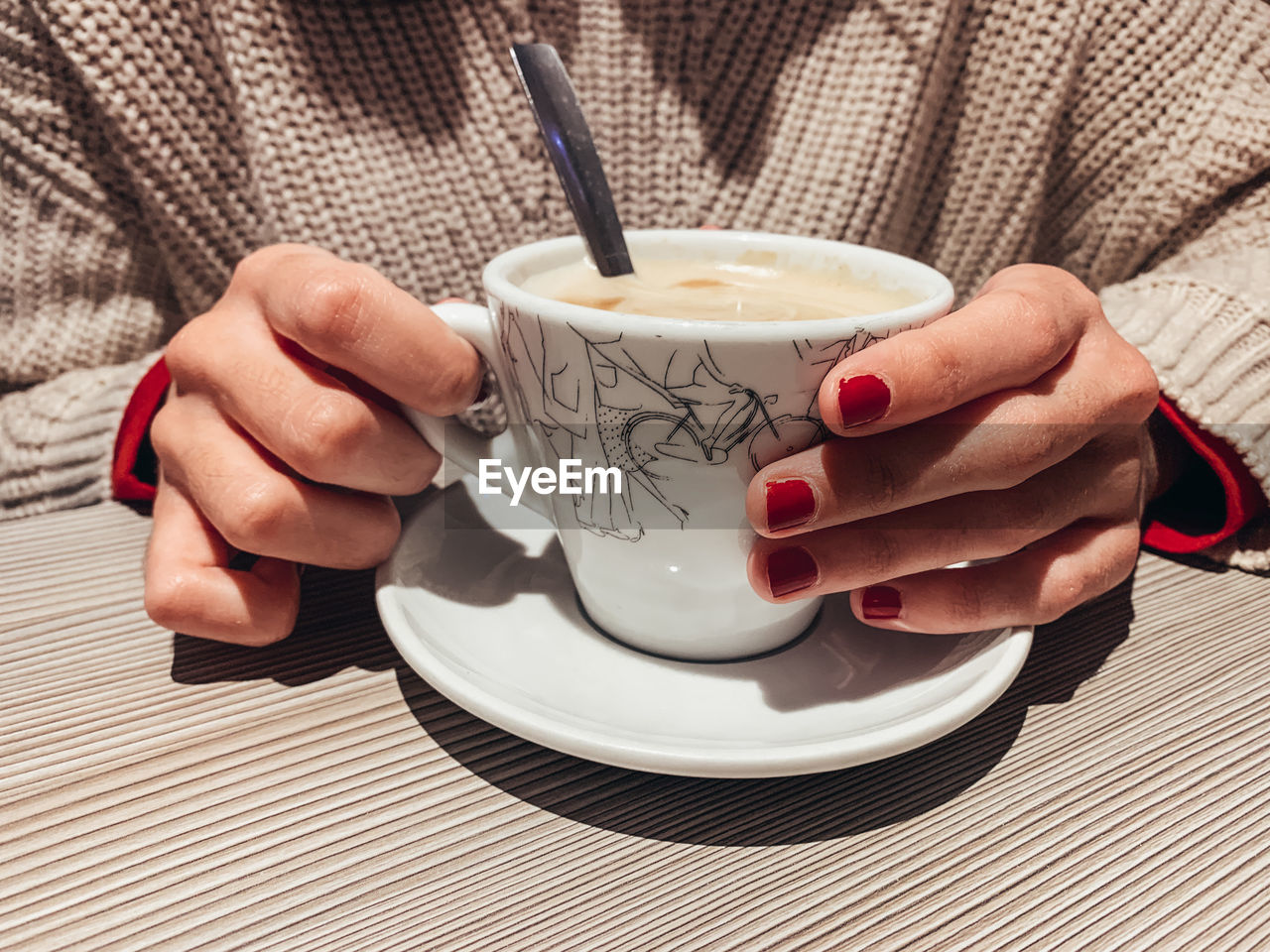 CLOSE-UP OF HAND HOLDING COFFEE CUP AND SPOON ON TABLE