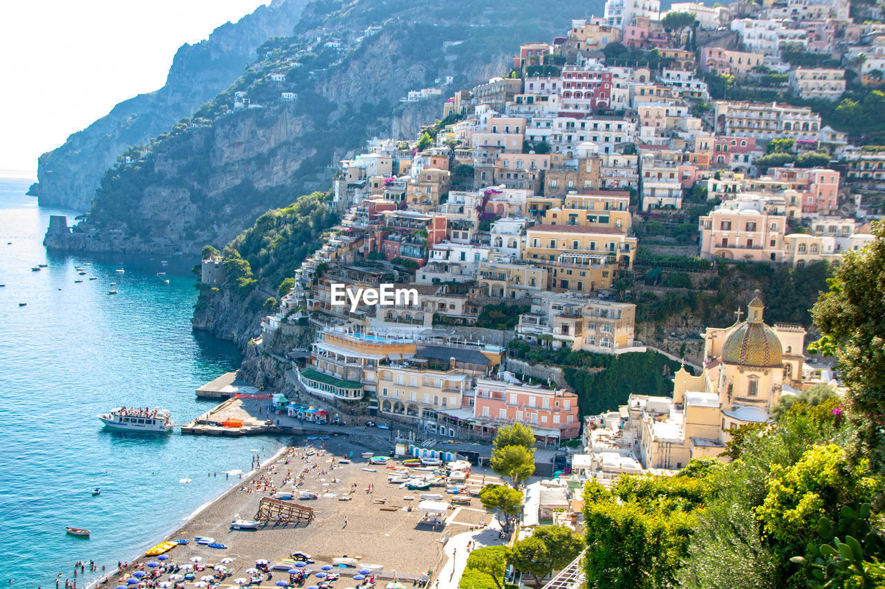 HIGH ANGLE VIEW OF BUILDINGS AND SEA AGAINST MOUNTAINS