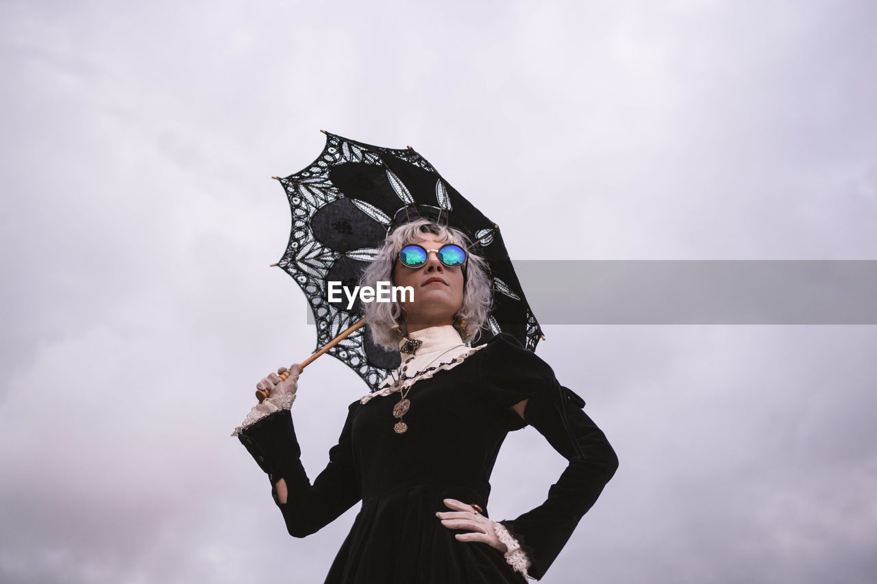 Low angle view of woman holding umbrella while standing against cloudy sky