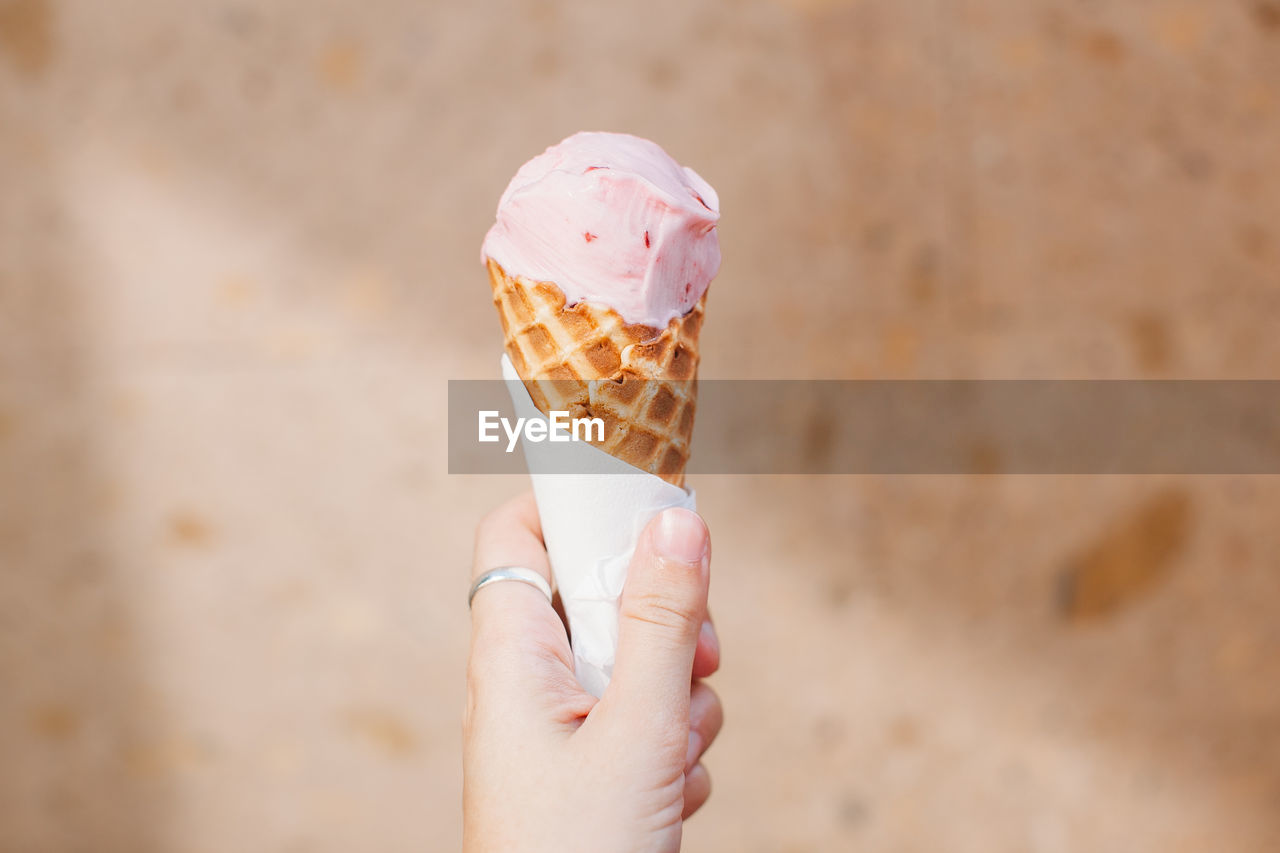 Cropped image of person holding ice cream against wall