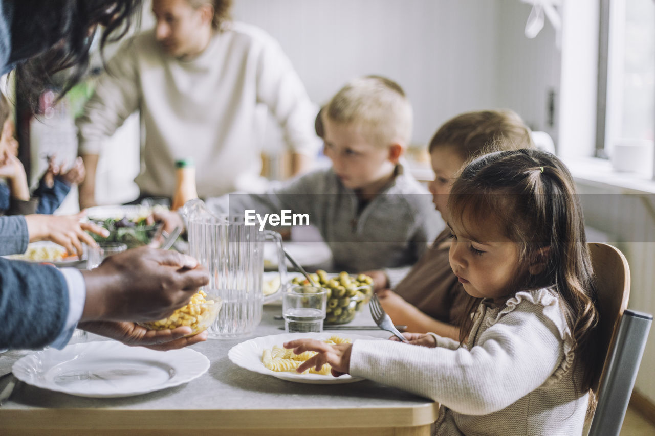 Teacher serving food to male and female students for breakfast in day care center