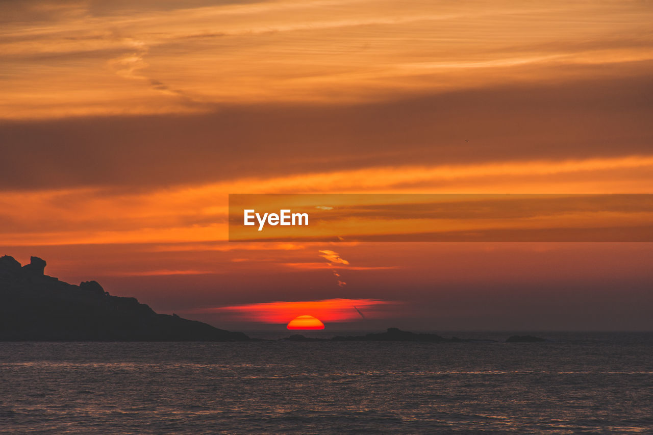 Scenic view of sea against dramatic sky during sunset