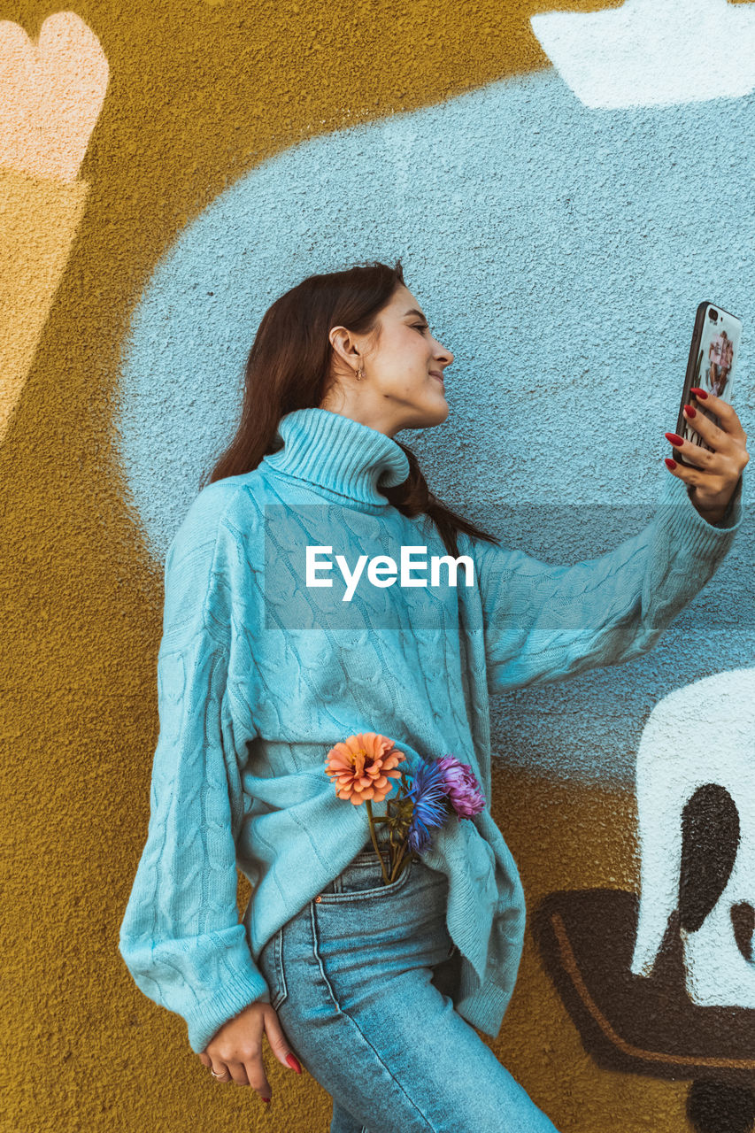 Midsection of woman using mobile phone against wall