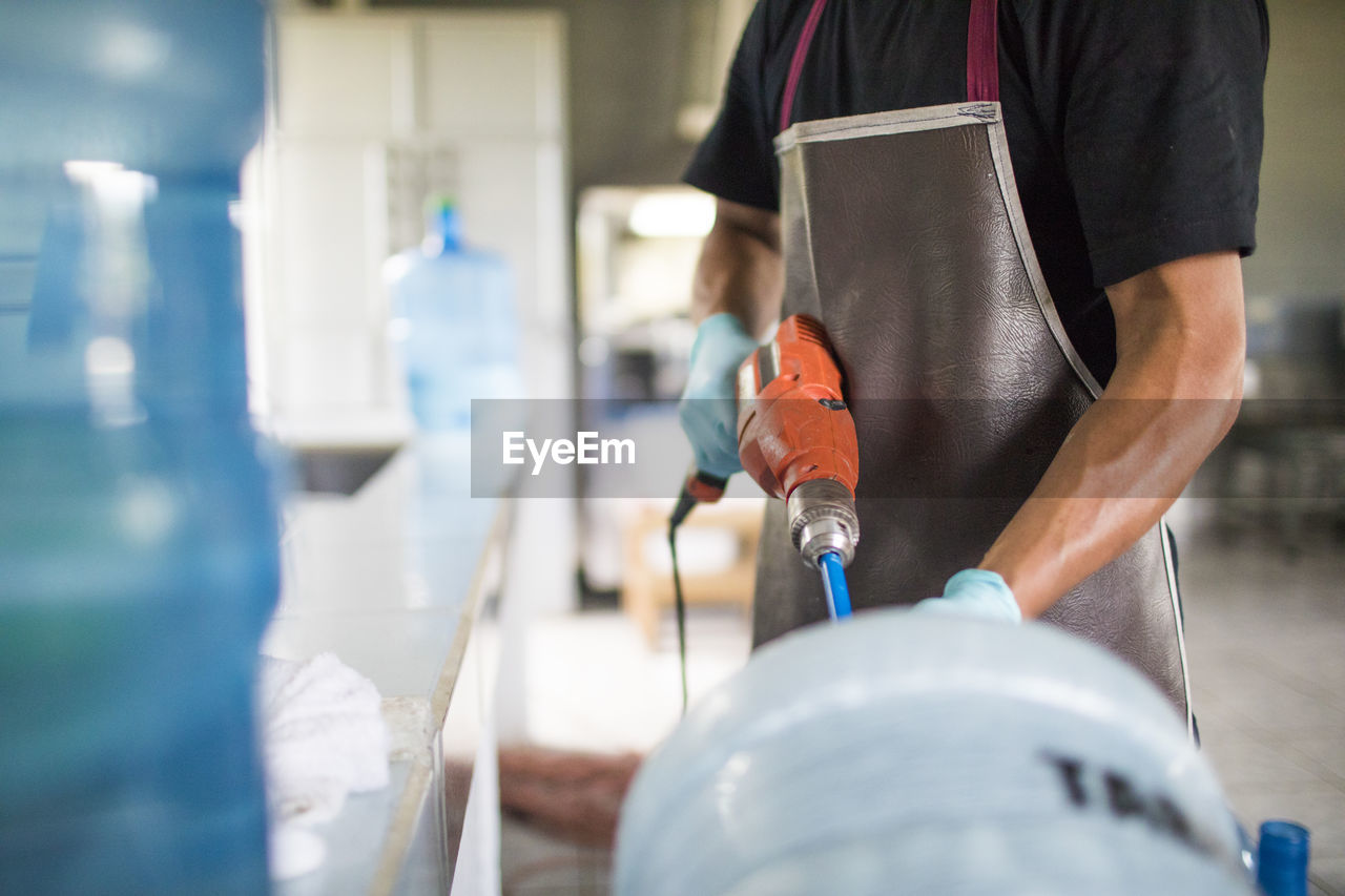 Worker uses a power drill to wash out a drinking water jug for re-use.