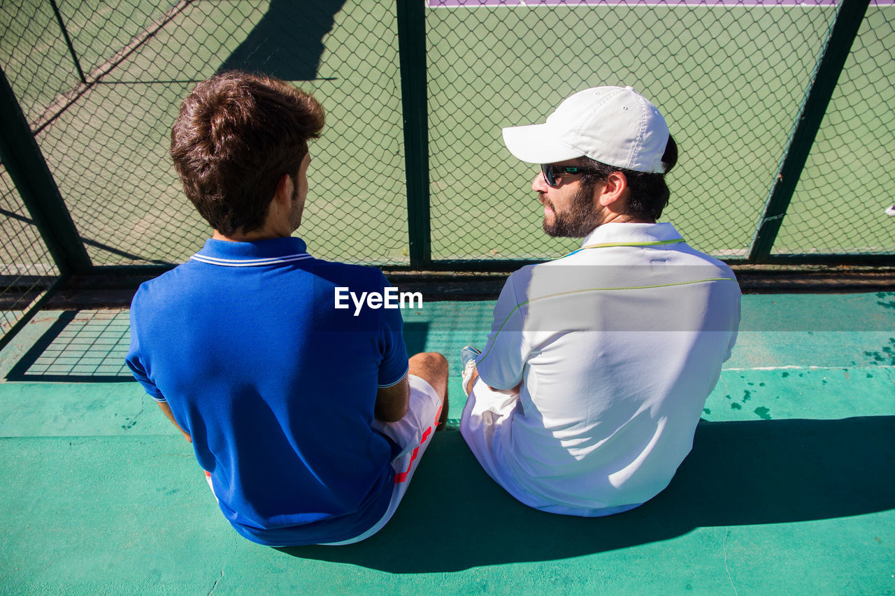 Tennis players sitting against net at court