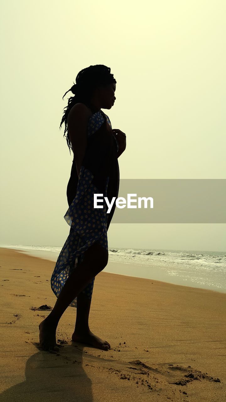 Side view of girl standing on beach against clear sky