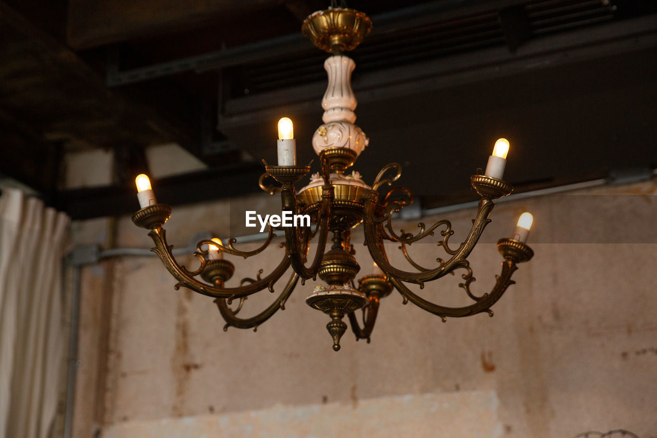 LOW ANGLE VIEW OF ILLUMINATED CHANDELIER HANGING FROM CEILING