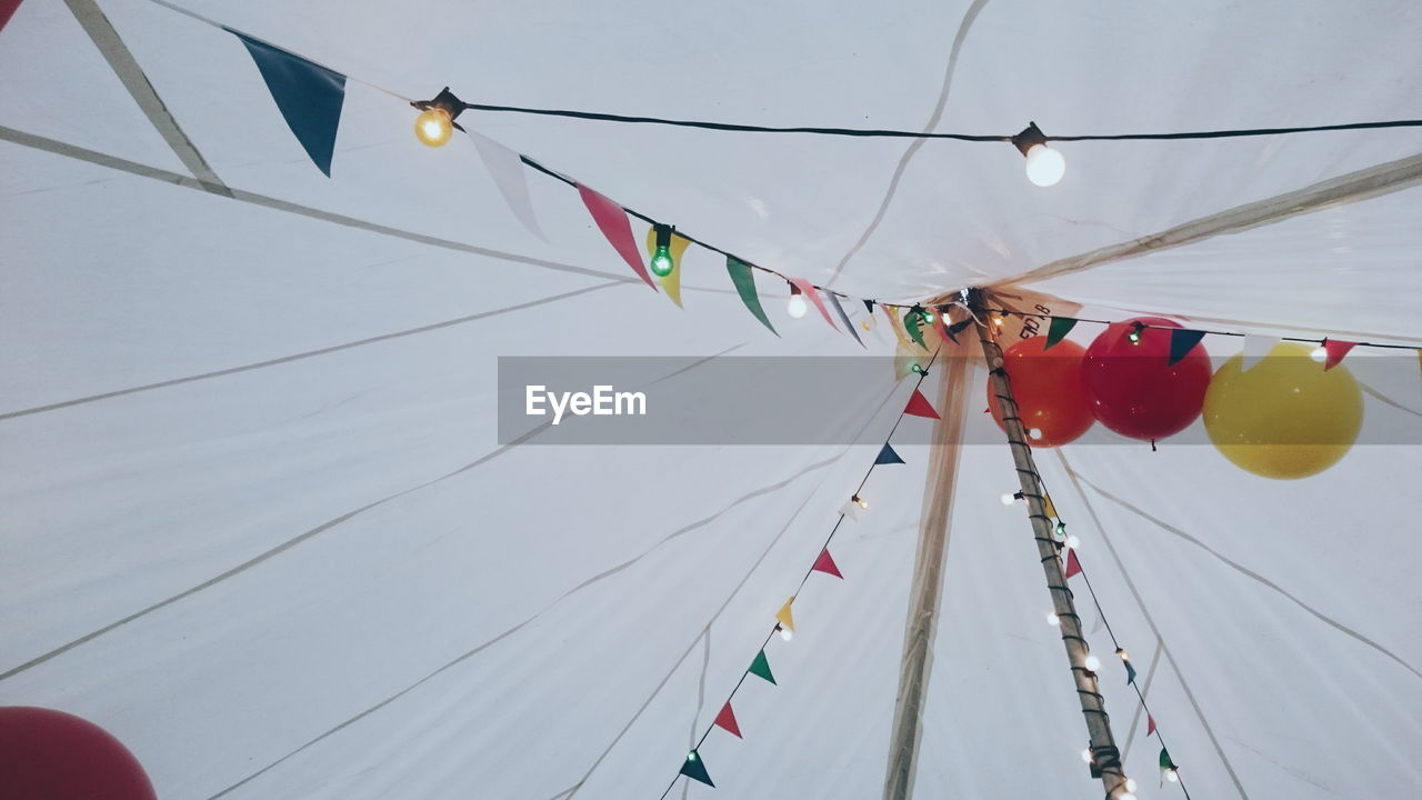 Low angle view of bunting and string light decoration against sky