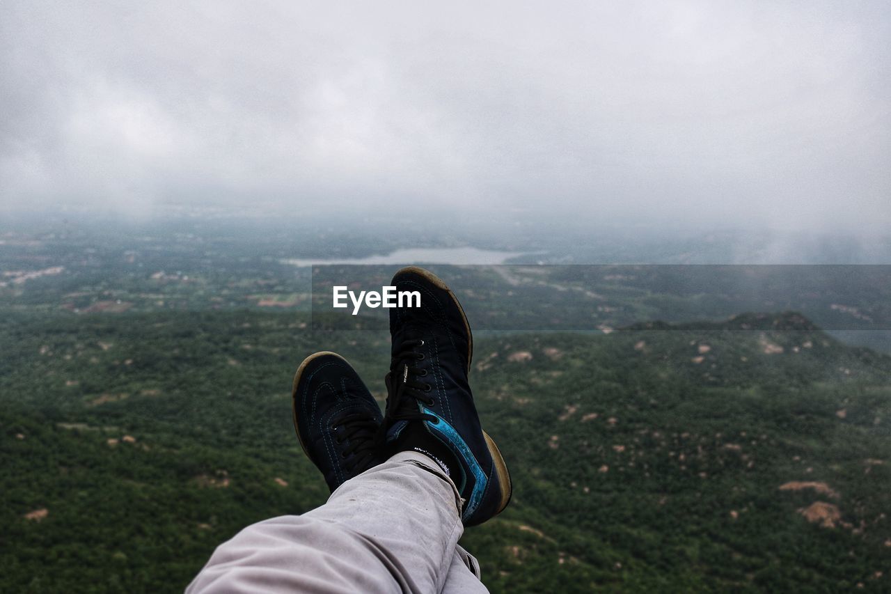 Low section of person on mountain against cloudy sky
